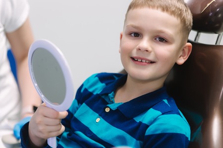 Little boy sitting in dantist chair with mirror. Male patient look at his teethの写真素材