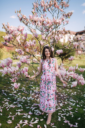 Charming girl stand by the beautiful pink magnolia tree outside. Gorgeous ladyの写真素材