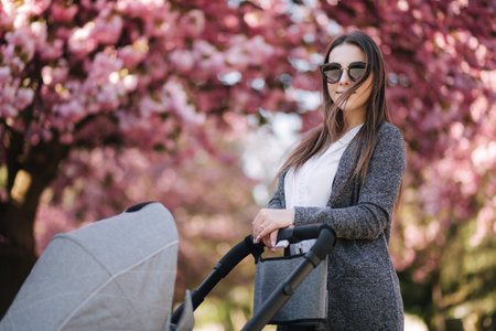 Portrait of mom stand with stroller in the park. Happy young mother walking with baby. Background of...