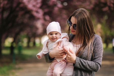 Beautiful mom walk with her baby girl on hands in the park. Pink backgroundの写真素材