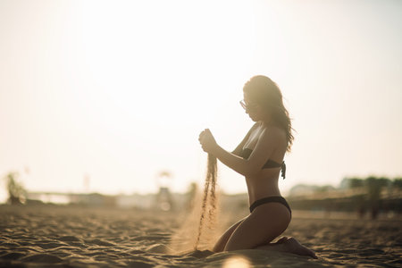 Sexy girl sunbathing on a beach and plays with sandの写真素材