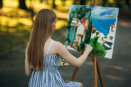 Back view of beautiful blond hair girl drawing a picture in the parkの写真素材