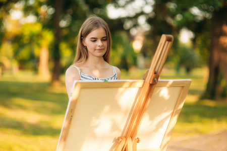 Blond hair girl in dress drawing a picture in the parkの写真素材