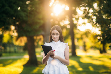 Young female teacher with tablet outside. Modern teacher in the park. Woman wears glasses