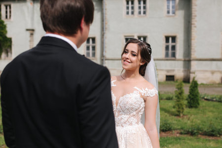 Newlyweds are walking in the park near the big castle. Beautiful bride with handsome groom