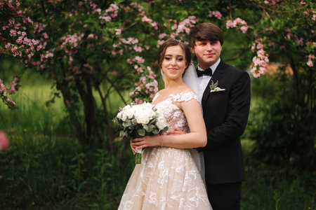 Handsome groom hug his beautiful bride. Newlyweds walking in the park. Brown hair woman in elegant...