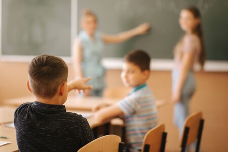Group of school kids with pens and notebooks writing test in classroom. education, elementary school, learning and people conceptの写真素材