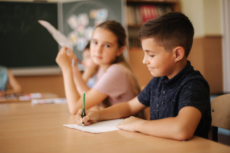 Group of school kids with pens and notebooks writing test in classroom. education, elementary...