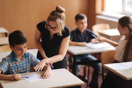 Teacher helping school kids writing test in classroom. education, elementary school, learning and people conceptの写真素材