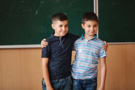 Two school boys stand in front of balckboard in class room