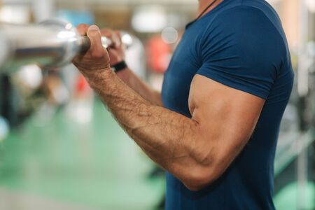 Close up of young athlete trains in the gym. Trians biceps muscules using barbellの写真素材