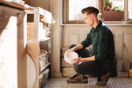 Man potter looking for ware for a work. Young man potter in his workshop. Handsome man workの写真素材