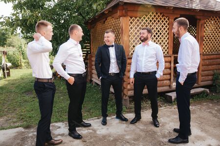 Handsome groom with his groomsman on the backyard. Five man. Groom dressed in suit, gromsmen in white shirt. Funny guys on the weddingの写真素材