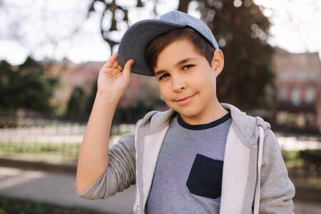 Stylish little school boy in blue cap posing outside for photo. Boy walking in the city in sping summer weatherの写真素材