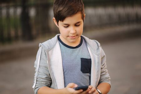 Young boy playing with smaptphone. Schoolboy using mobile phone on the streetの写真素材