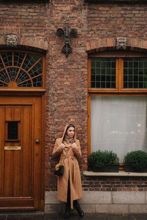 Stylish woman in brown coat standing on the bridge in Bealgium, Brugge. Female put on a hoodの写真素材