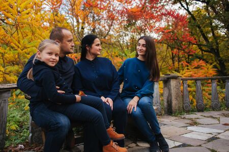 Portrait of happy family sitting on the bench in the forest. Autumn weather and colorful treesの写真素材