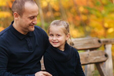 Portrait of happy family sitting on the bench in the forest. Autumn weather and colorful treesの写真素材