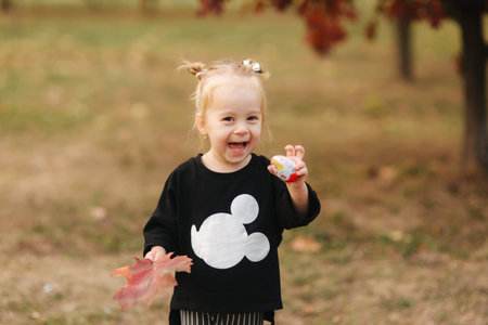 Happy little girl walking in the park in autumn. Beautiful female kid on yellow background