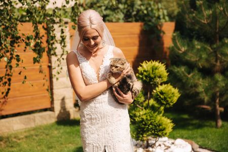 Beautiful blond hair bride with het pet on the back yard. Cute cat in brides handsの写真素材