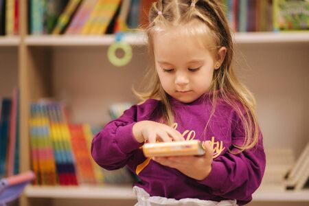 Adorable little girl shopping for toys. Cute female in toy store. Happy young girl selecting toyの写真素材