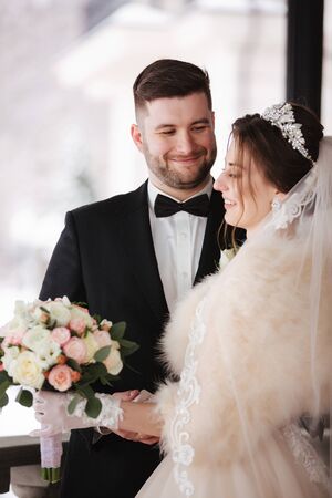 Young bride with groom stand on balcony. Bride in fur coat in winter timeの写真素材