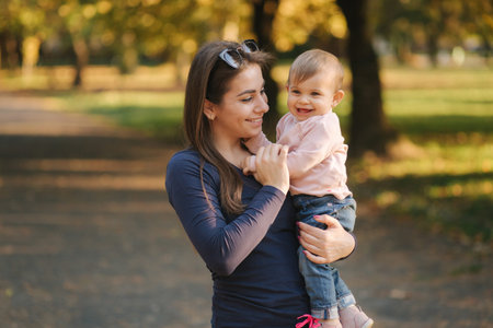 Adorable laughing baby girl on moms hands in autumn park. Close up on mother and daughter. Happy...