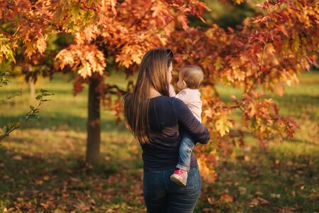 Mother with her little baby girl stand in front of red tree. Autumn park.の写真素材