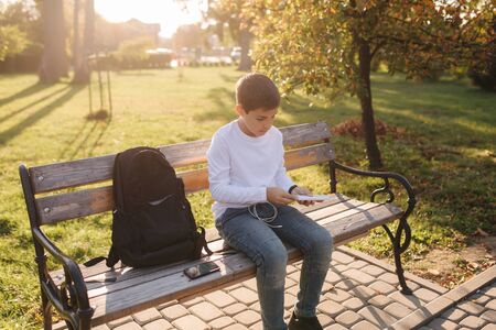 Handsome teenage boy take from his backpack powerbark for charging smarphone. Cute boy in the park in autumn timeの写真素材