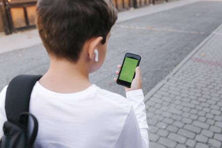 Mock up of teenage boy with wireless headphones use phone otside. Green screenの写真素材