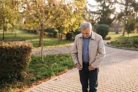 Elderly man zip a fly on jacket. Old bearded man in autumn park.の写真素材