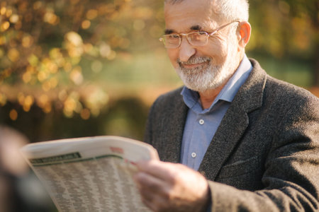 Senior man read a newspaper in the park. Background of yellow tree in autumn