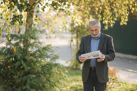 Senior man read a newspaper in the park. Background of yellow tree in autumn