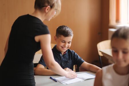 Teacher helping school kids writing test in classroom. education, elementary school, learning and people conceptの写真素材