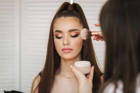 Female makeup master use a powder brush. Beautiful model in beauty studio. Professional make up artist finish fashion maleup. Background of white folding screenの写真素材