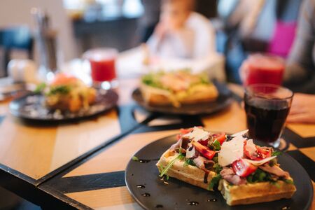 Waffles sandwich with bacon chiken and frech salad on black plate. Background of wooden tableの写真素材
