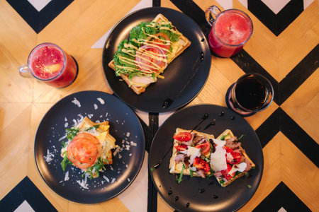 Waffles sandwich with bacon chiken and frech salad on black plate. Background of wooden table