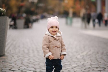 Happy baby girl walking in the city in autumn time. Cute baby in brown coat and jeansの写真素材