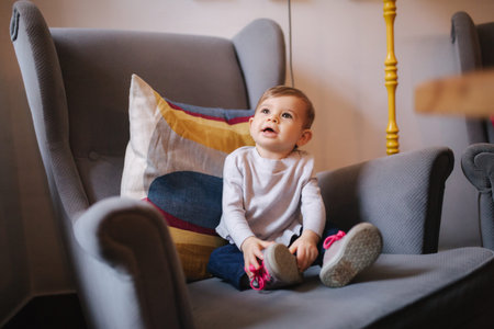 Cute baby girl sitting on big armchair and smile