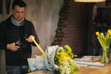 Male make spring bouquet. Man tying bouquet of flowers with yellow ribbon. Beautiful flower composition of yellow flowers.の写真素材