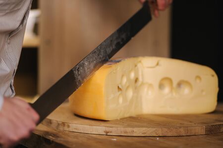 Young worker slice cheese maasdam on wooden board in cheese shopの写真素材