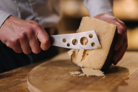 Man slicing little piece of cheese for taste. Young worker use special knife for cheese.の写真素材
