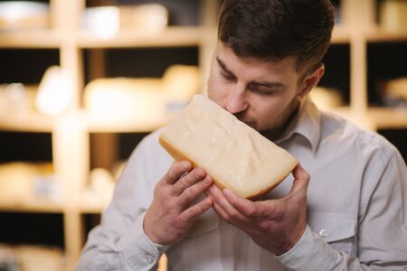 Portrait of Handsome bearded man sniff aged cheese in shopの写真素材