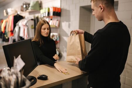 Attractive woman is giving a credit card to shop manager. Customer give credit card to assistant and smiling while doing shopping in boutiqueの写真素材