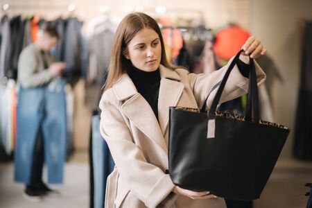Young woman trying on black bag. Woman in boutiqueの写真素材