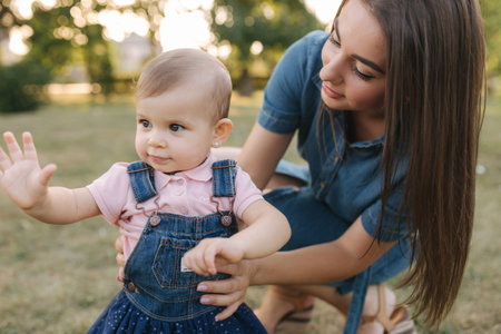 First step of adorable little girl in summer park. Mom and daughter walking