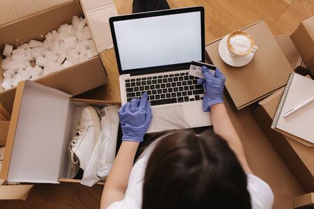 Top view of women in mask and gloves working at home on laptop on wooden floor with parcel. Selling, buying online on quarantine. Coronovirus conceptの写真素材