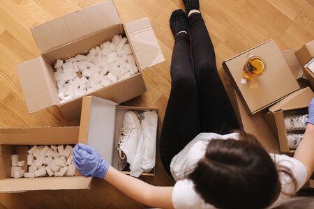Top view of women in mask and gloves working at home on laptop on wooden floor with parcel. Selling, buying online on quarantine. Coronovirus conceptの写真素材