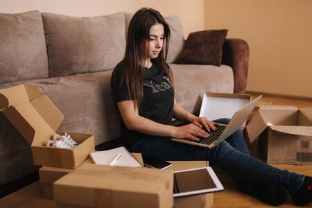 Happy young woman shopping online. Woman use laptop and tablet for searching new goods. Attractive girl surrounded by parcelsの写真素材