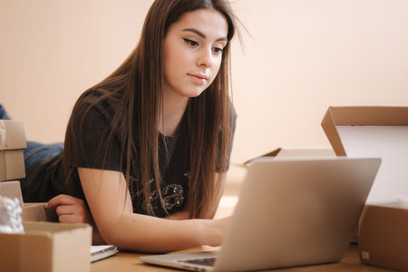 Young woman doing online shopping at home. Female lying on the wooden floor with different parcel....